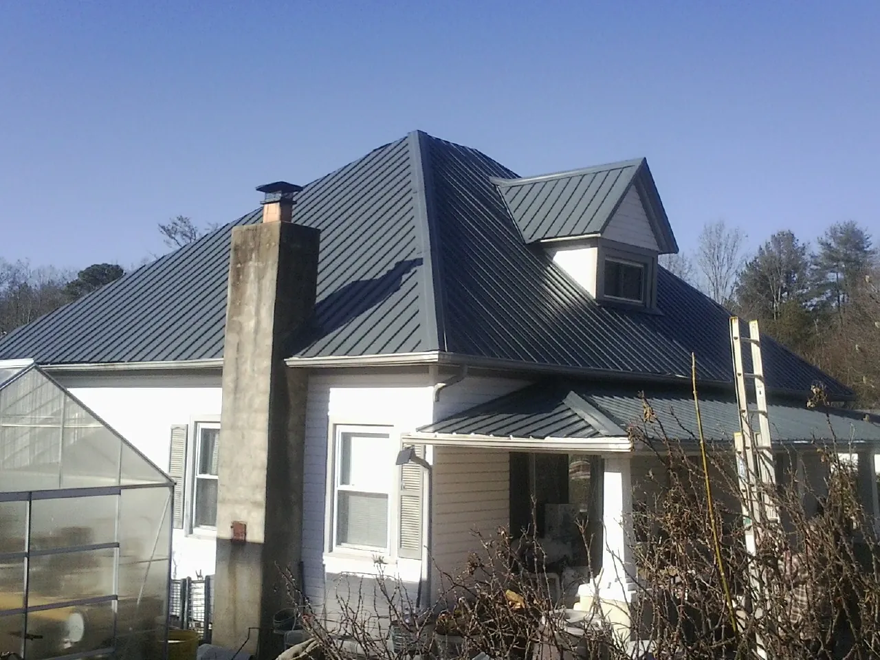 Dark blue standing seam metal roof on a white farmhouse with dormer — Slate & Tile Roof Repair by Roofing Brothers in Gravity