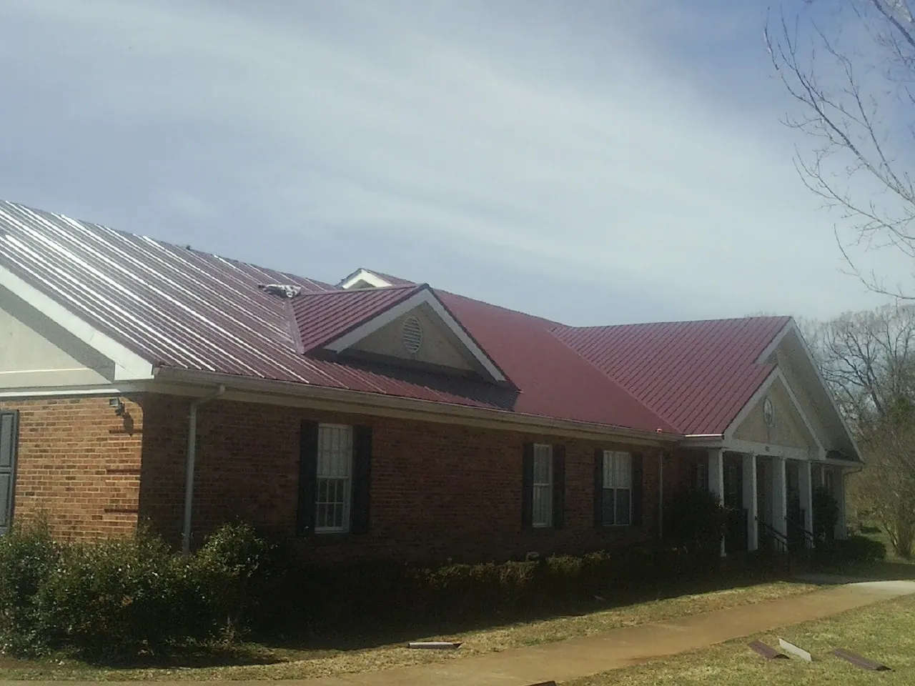 Red metal roof with gabled entries on a long brick building, from a Hail Damage Roof Repair job in Gravity
