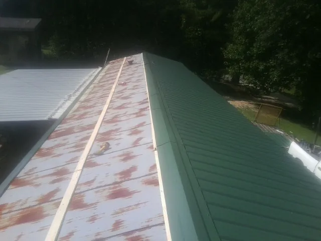 Old rusted panels beside newly installed green metal roofing — Wind Damage Roof Repair by Roofing Brothers in Gravity