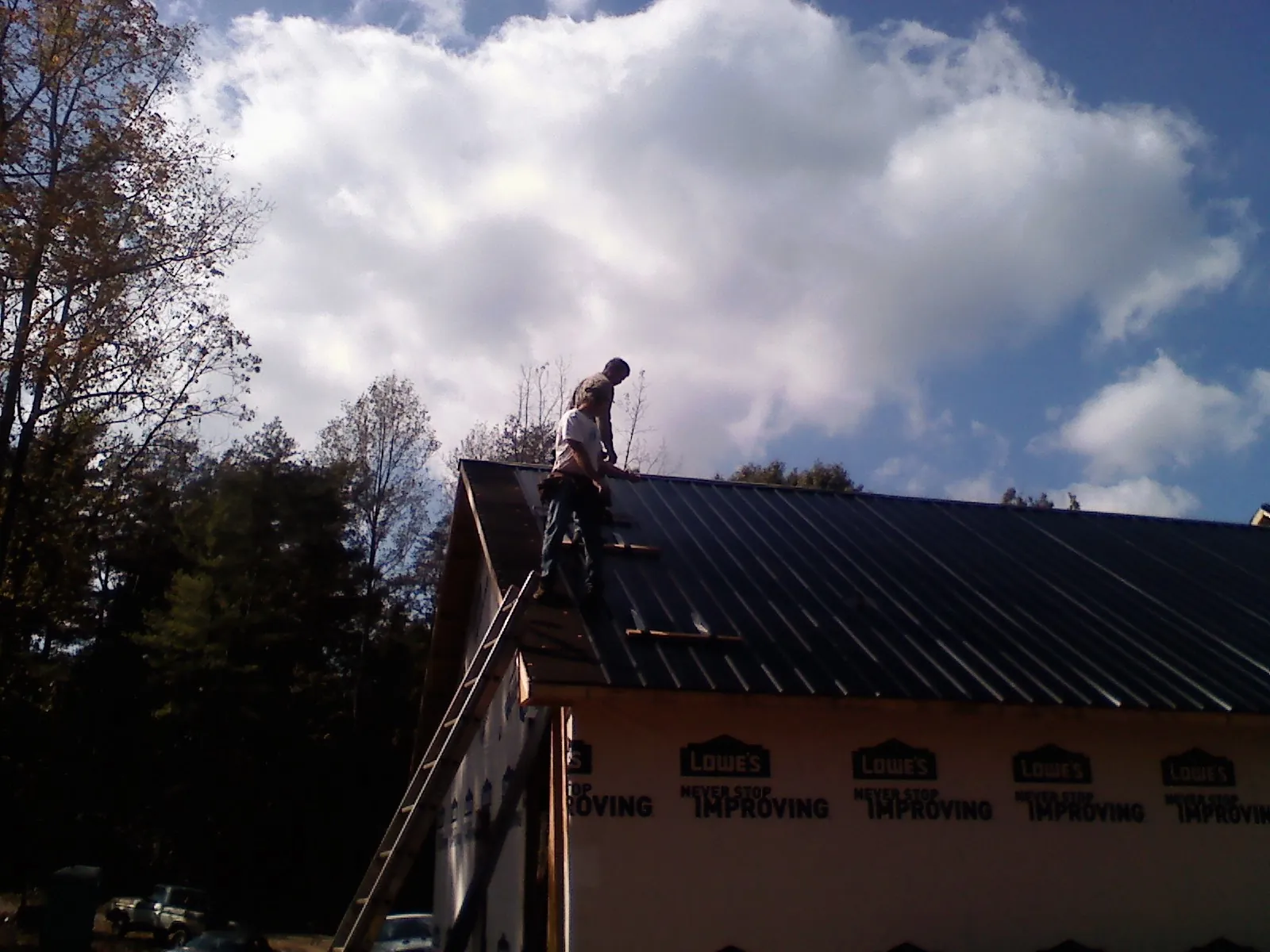 Roofer fastening dark metal panels high against a cloudy sky, from a Roof Inspection job in Gravity