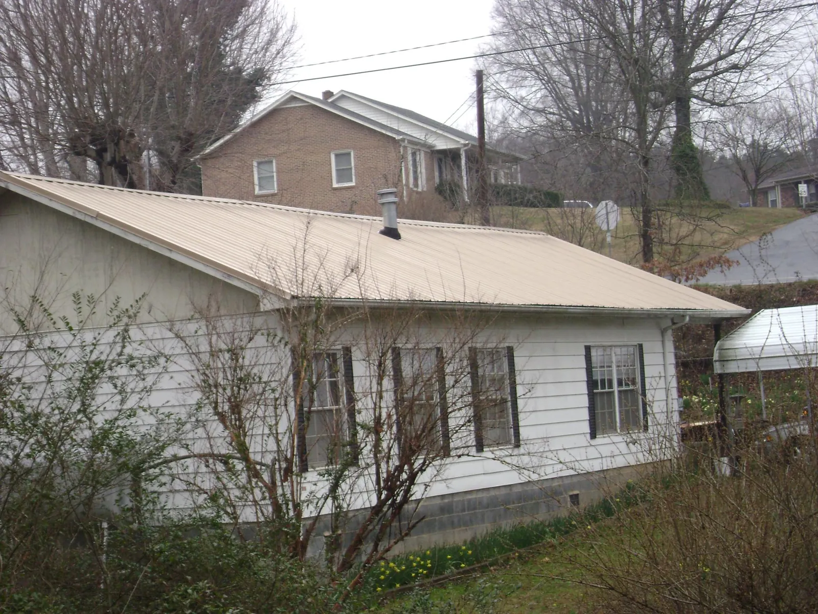 Tan metal roof on a white sided house set into a hillside — Commercial Roofing by Roofing Brothers in Gravity